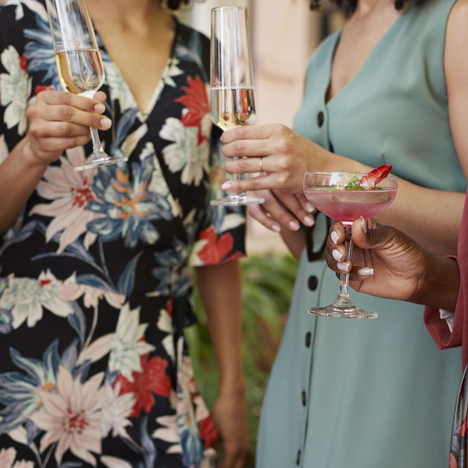 Closeup of Woman in Floral Wrap Dress and Blue Button-Down Dress Holding Champagne Coupes