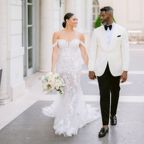 Bride in Lace Wedding Dress With Hair Bun Posing With Groom in Black in White Tuxedo