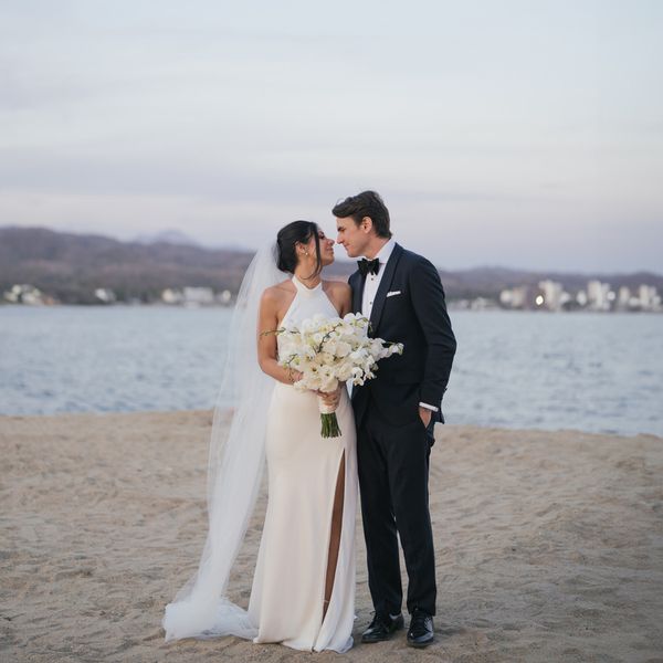 bride and groom couple portrait on sandy beach holding flower bouquet leaning in for a kiss