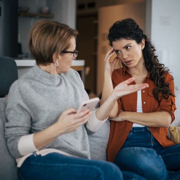 Woman Sitting on Couch and Holding Phone While Having Argument With Younger Woman