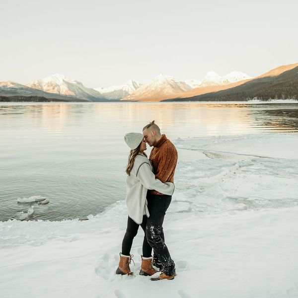 Couple Embracing One Another While Standing in the Snow in Front of Glacier for Winter Engagement Photo Shoot