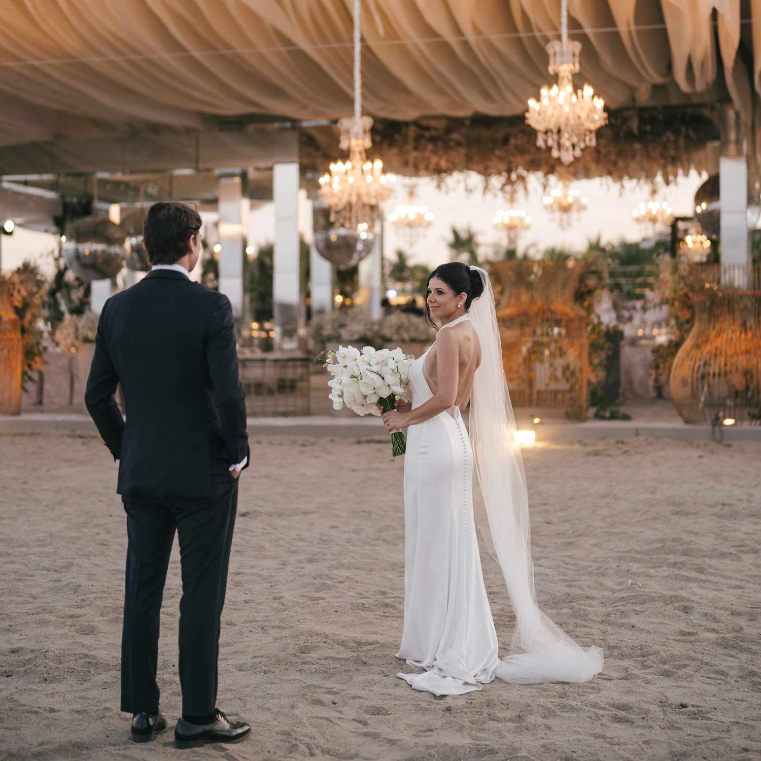 Bride and Groom Looking at Each Other and Standing on the Beach in Front of Glamorous Tent