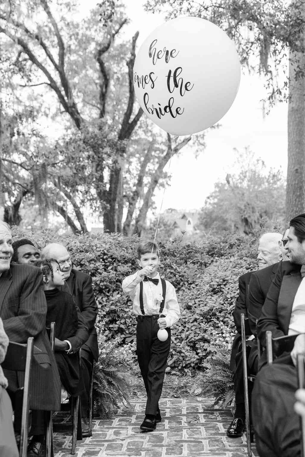 A ring bearer holding an oversized balloon while walking down the aisle