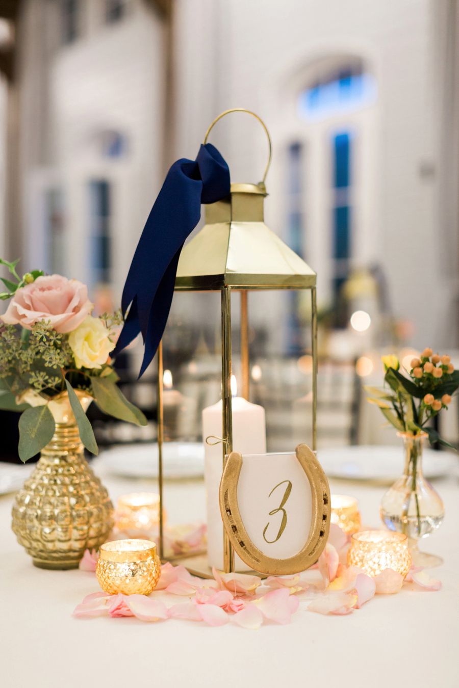 gold lantern with navy ribbon, pink petals, and gold horseshoe number sign