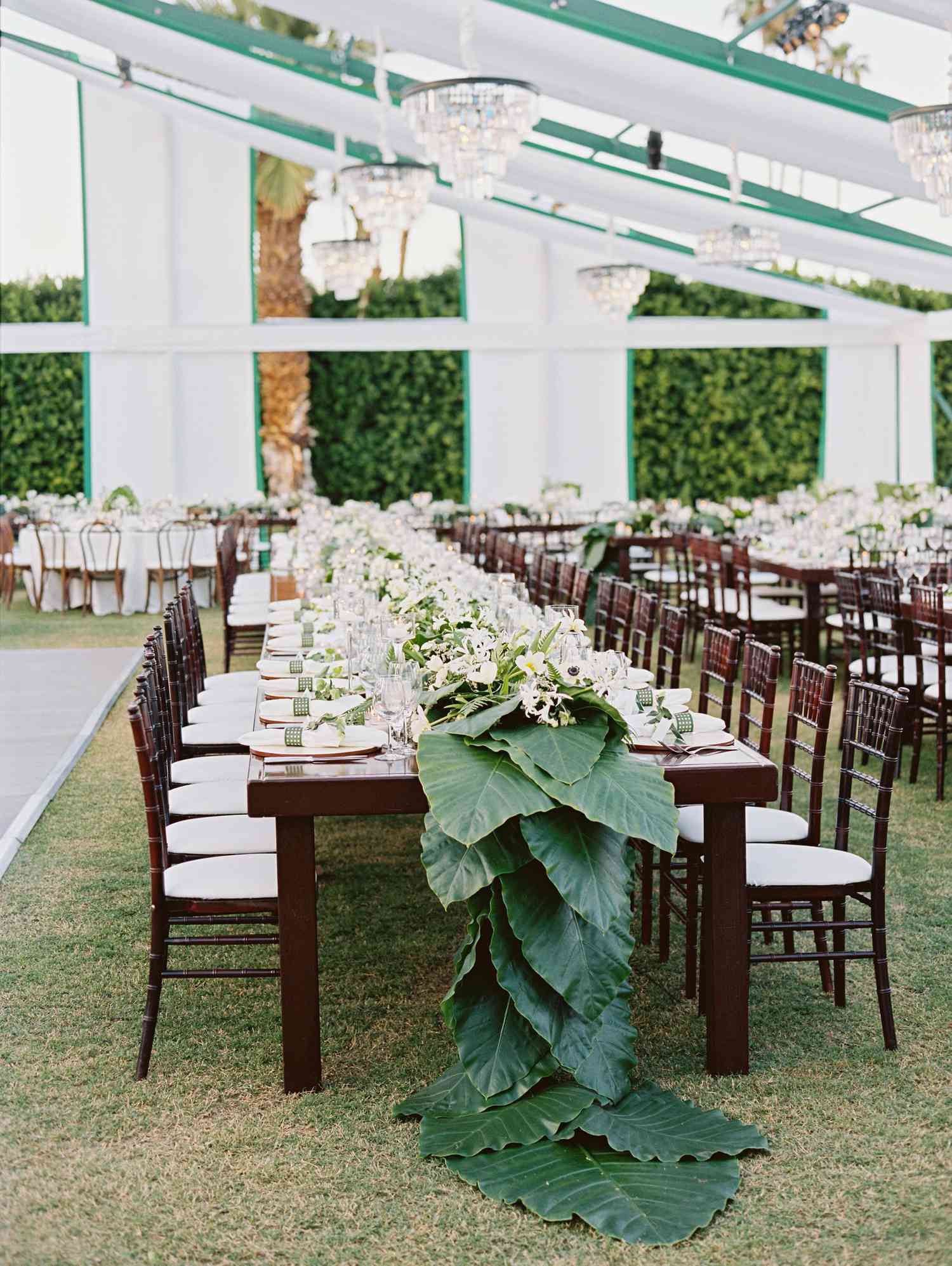 tropical leaves table runner on long dark wood tables and white place settings