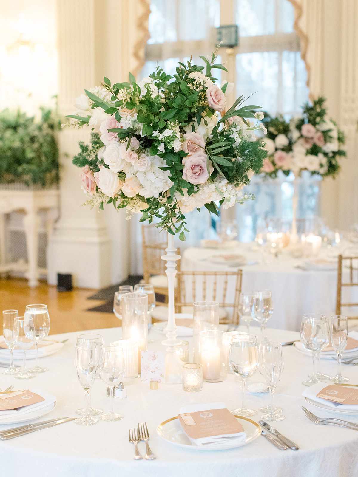 Tall wedding centerpieces on round table with roses, greenery, and hydrangeas