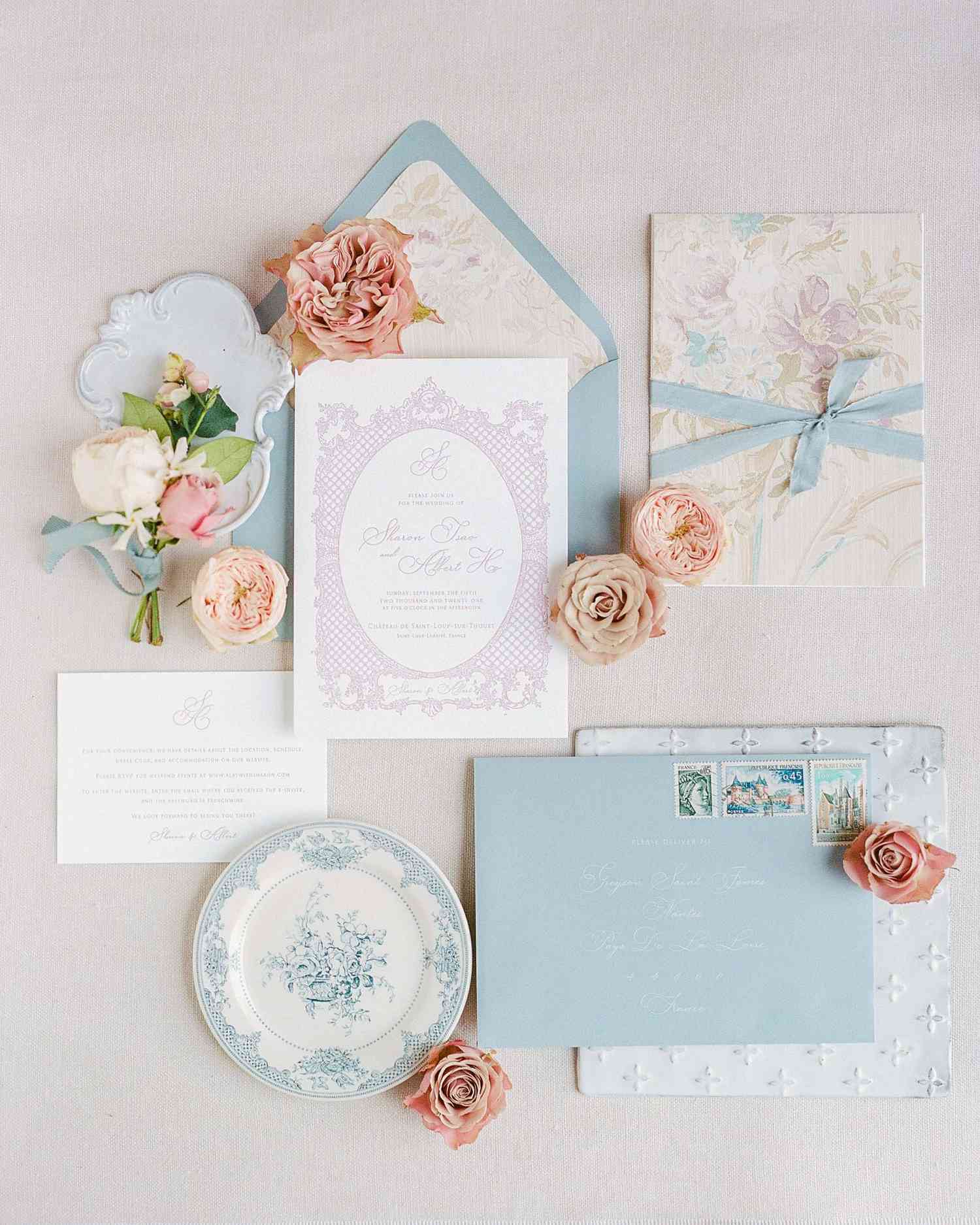 Elegant invitation suite in pastel blue and lavender with floral illustrations and light blue ribbon