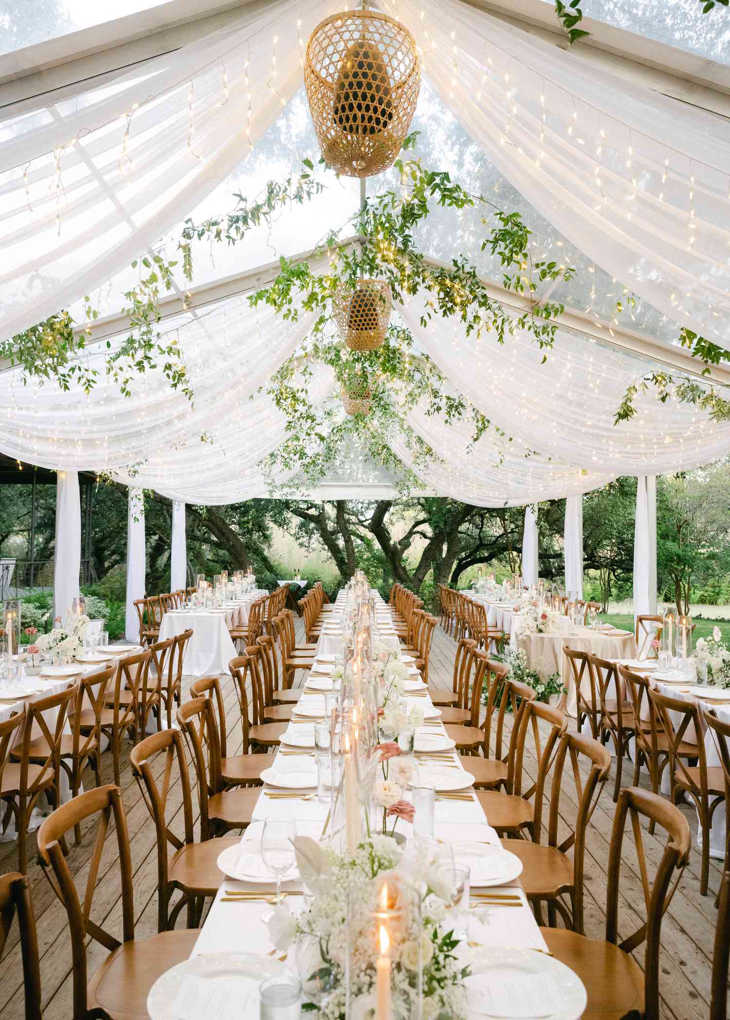 tented reception suspended with string lights, greenery, rattan lanterns, and sheer draping