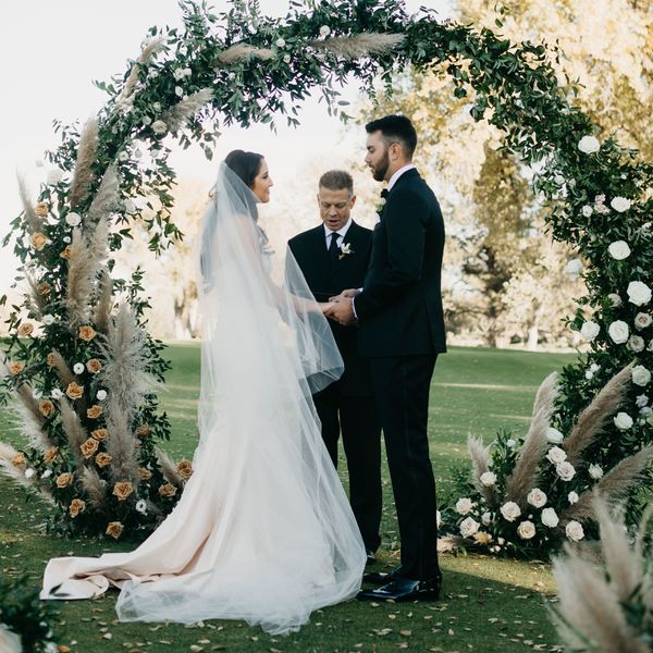 bride and groom standing with their wedding officiant in front of circular greenery arch