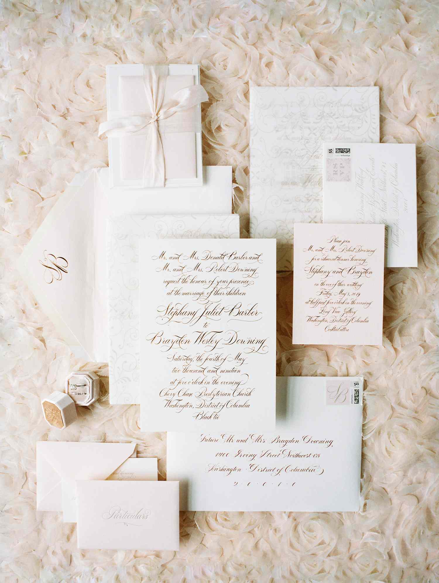 A white and pale pink themed fall invitation suite on a bed of tulle roses.