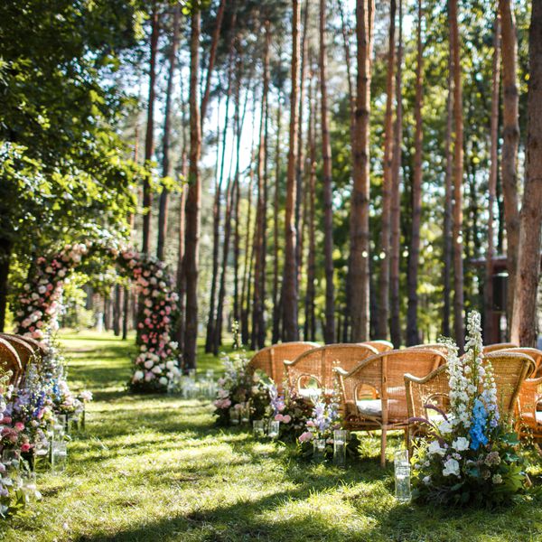 outdoor summer wedding with wicker chairs, delphinium floral arrangements, and flower arch at altar