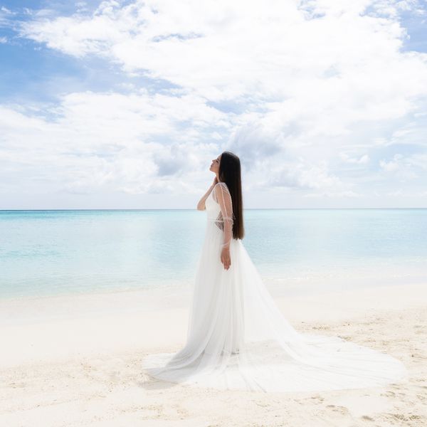 A bride in a white dress is standing on a snow-white beach