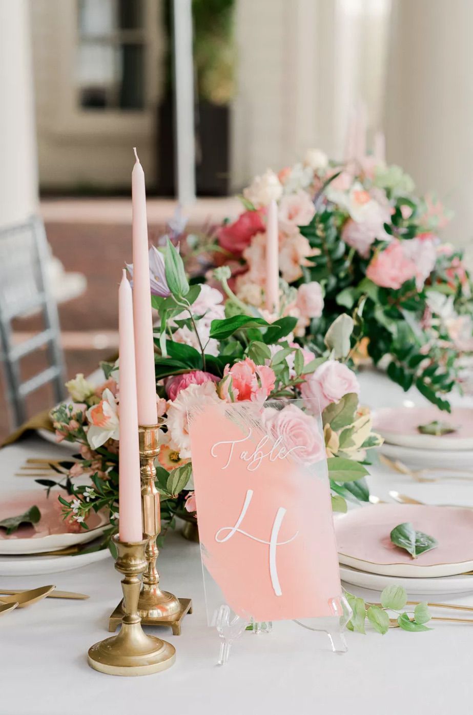 Pink acrylic table numbers, pink taper candles, and pink and green floral arrangements on wedding tablescape