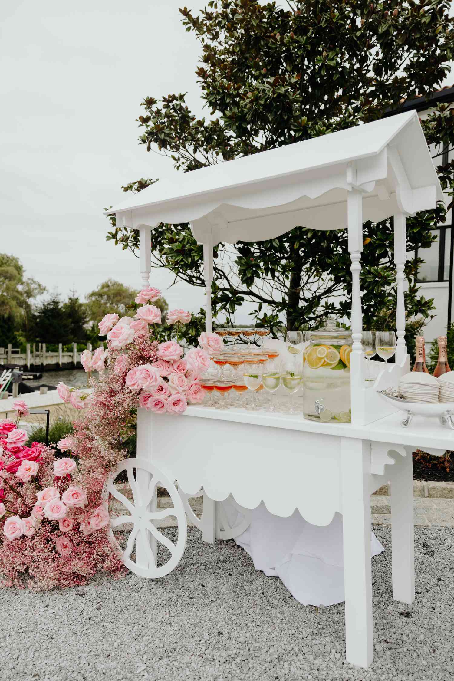 white cart with welcome cocktails and trailing rose floral garland at backyard wedding