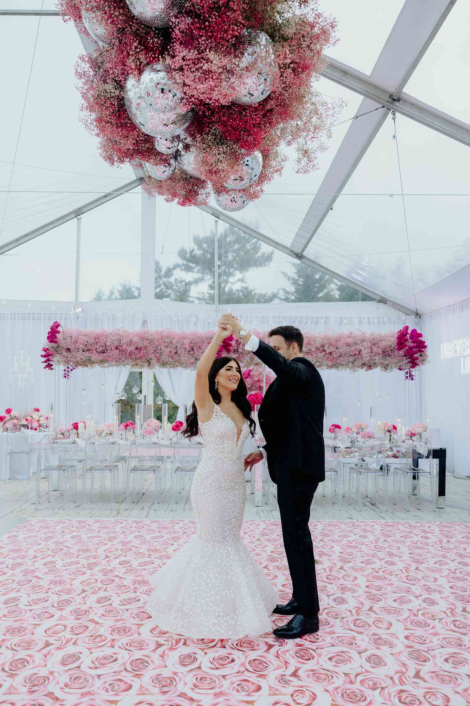 Bride and groom practice their first dance on rose dance floor underneath pink baby's breath installation