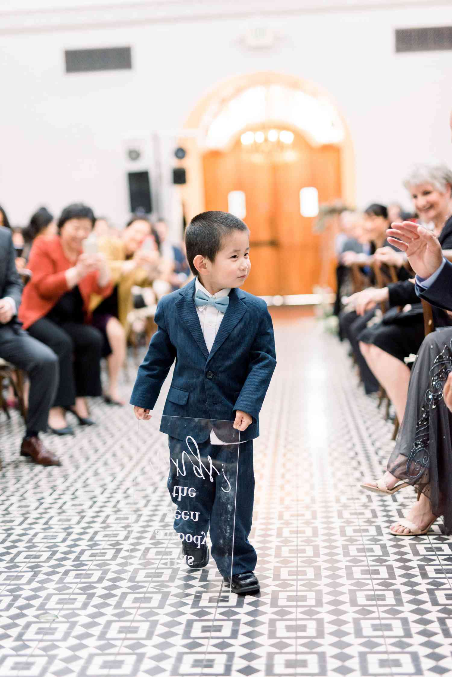 Ring Bearer Holding Lucite Sign at Indoor Ceremony