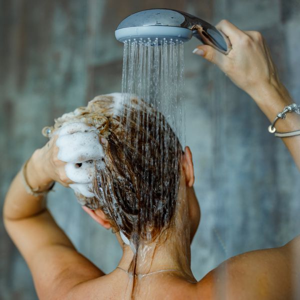 View of a woman washing her hair in the shower using thickening shampoo.