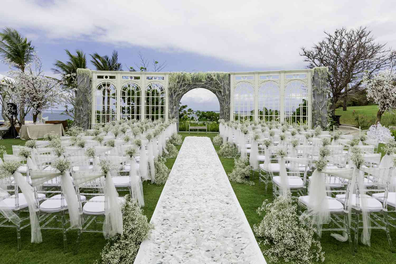 A white wedding ceremony with chairs, white flowers, and a white aisle in Bali
