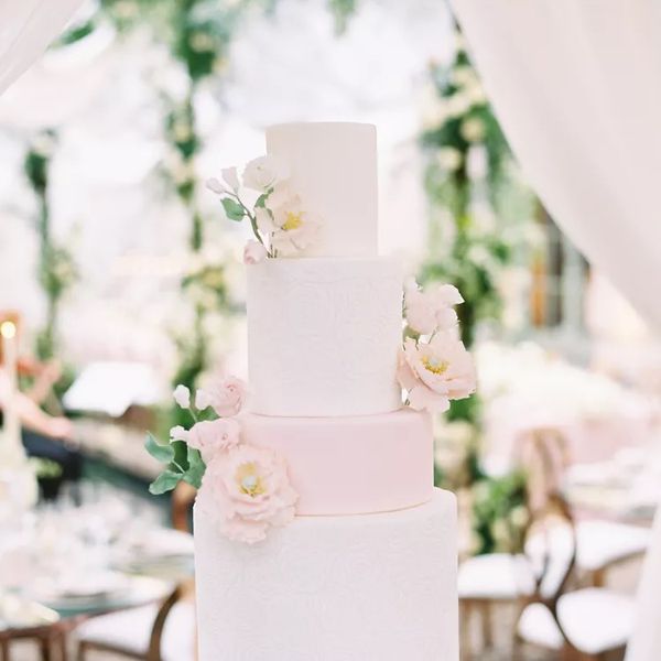 A four-tiered pink and white wedding cake covered in flowers at a tented wedding reception.