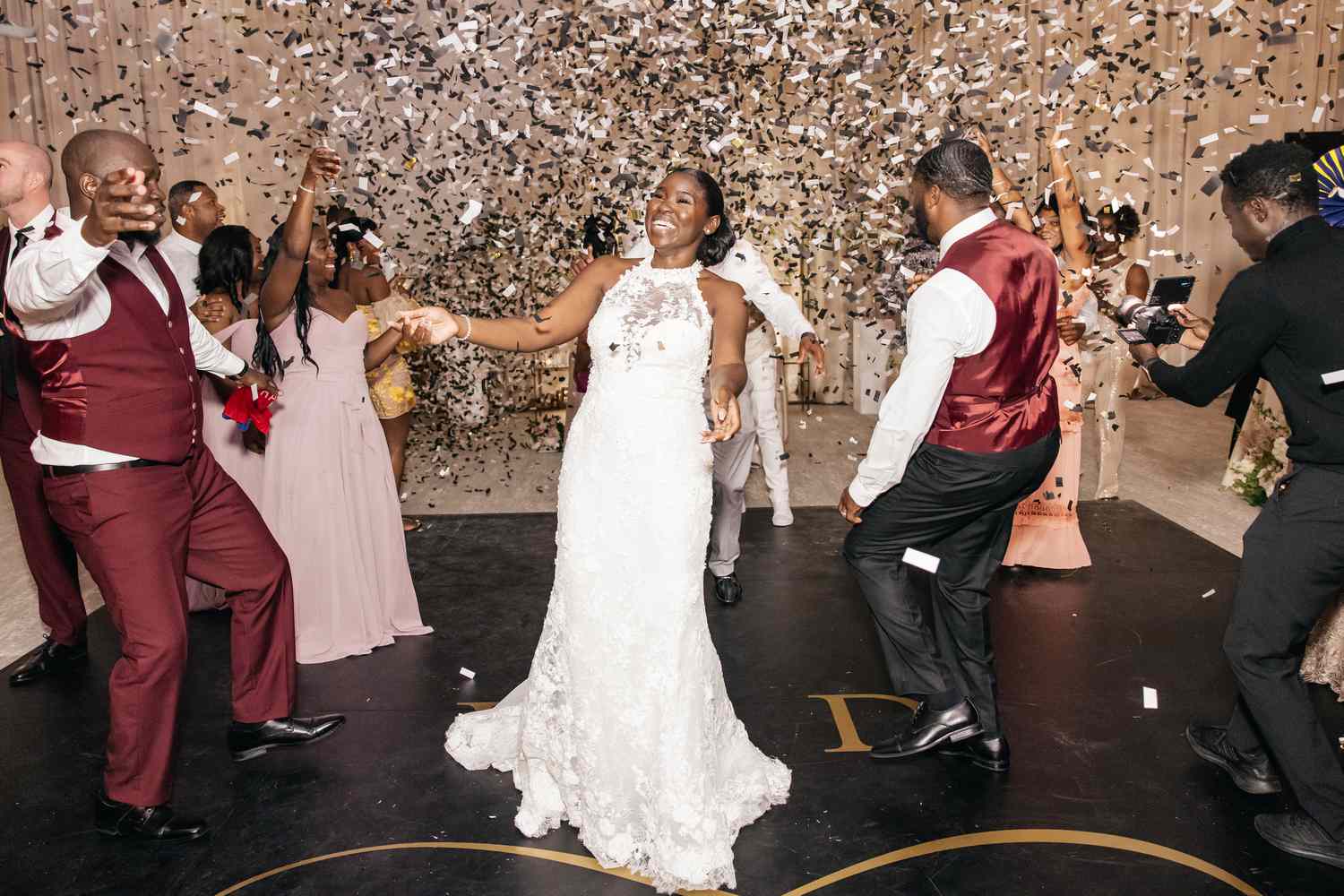 Bride and groom dancing underneath metallic confetti on a monogrammed dance floor with their guests