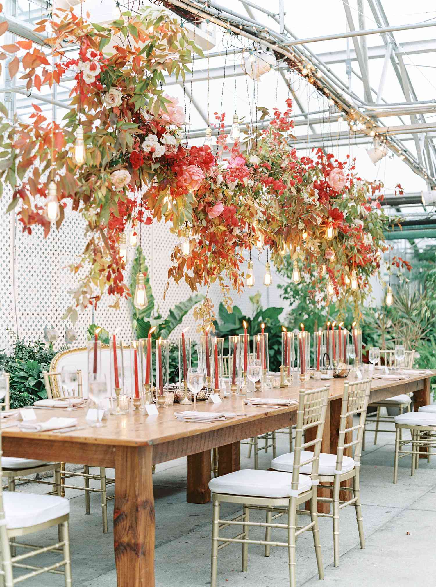 Floral and light bulb installation with flowers and greenery suspended above wedding reception seating