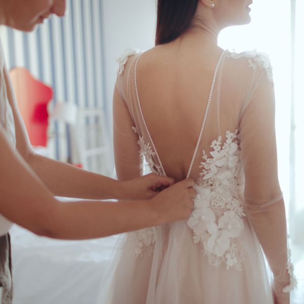 Woman Helps Bride Put On Wedding Dress
