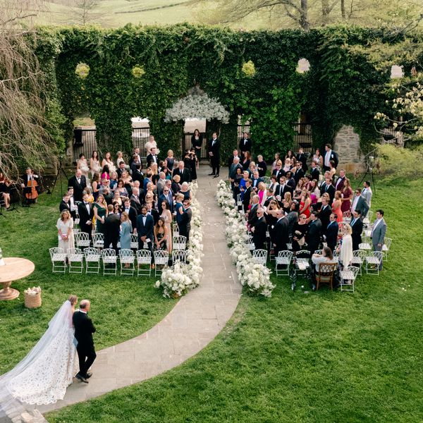 Bride and Father Walking Down Flower-Lined Aisle During Processional at Outdoor Wedding Ceremony