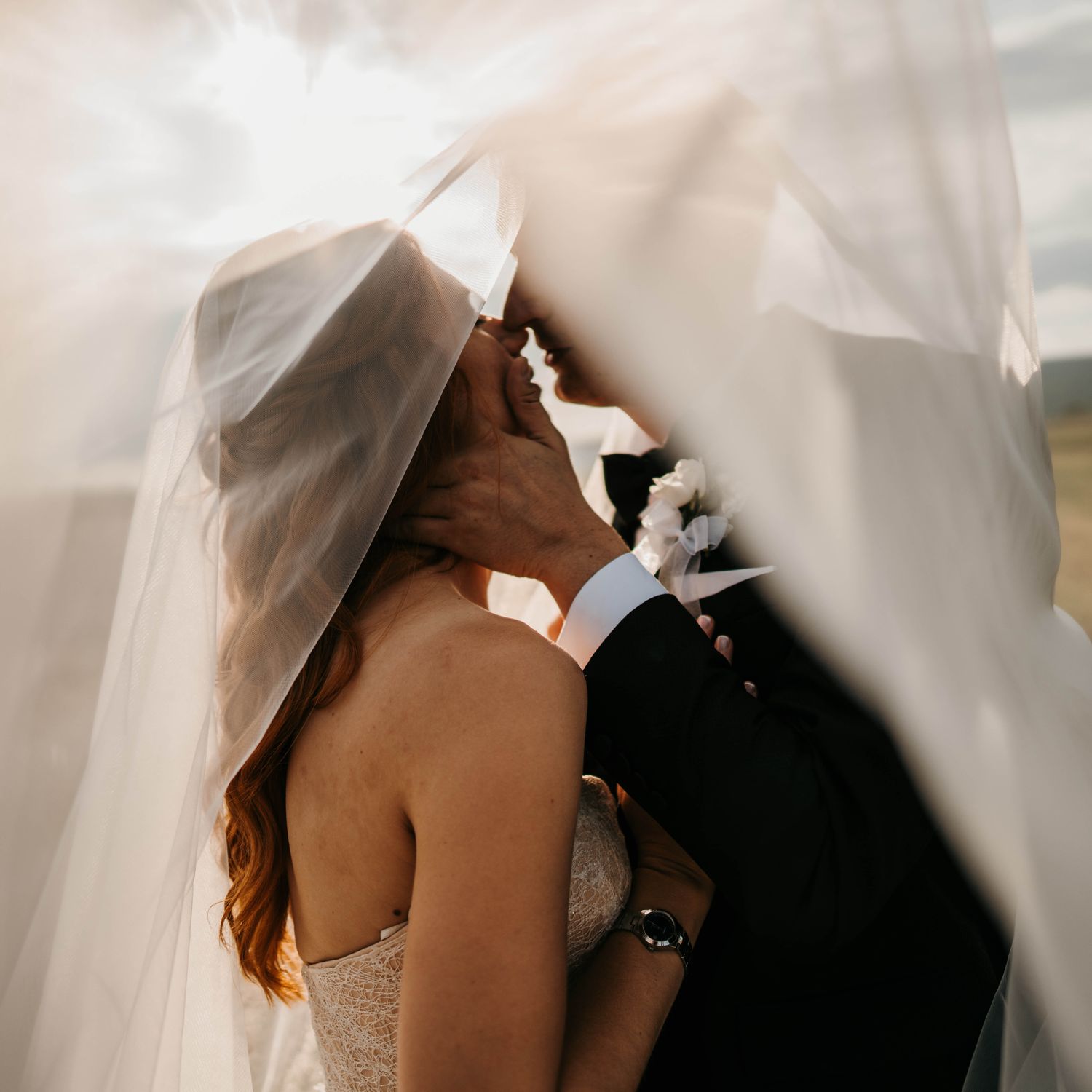 Bride and groom kissing tenderly under a long veil in nature