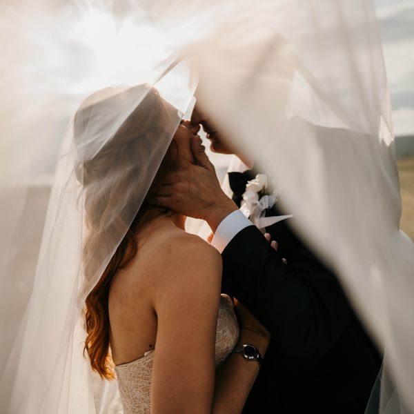 Bride and groom kissing tenderly under a long veil in nature