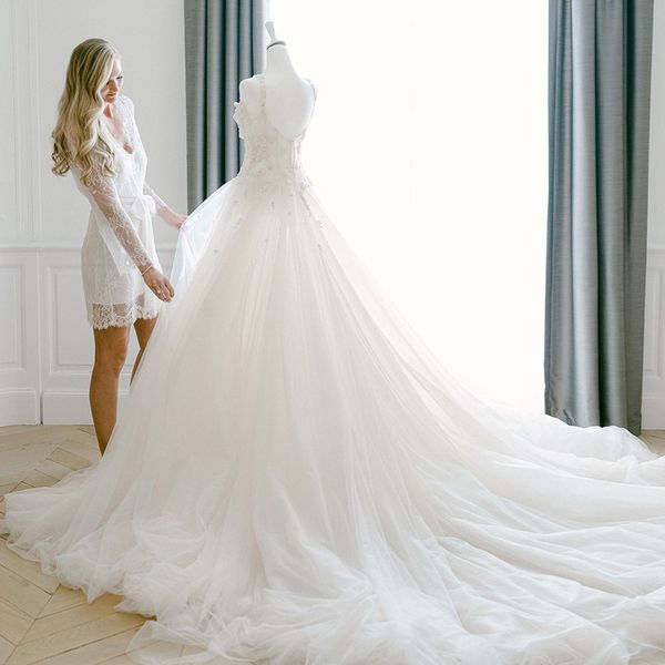 Bride in Lace Robe Looking at Ball Gown Wedding Dress on Mannequin