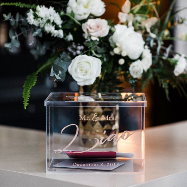 Acrylic Wedding Gift Box with Cards on White Table with White and Green Floral Arrangement Behind It