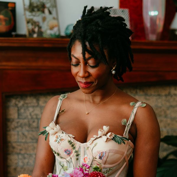Bride with locs pinned to the side in a lob, wearing a floral wedding dress and looking down at her bouquet