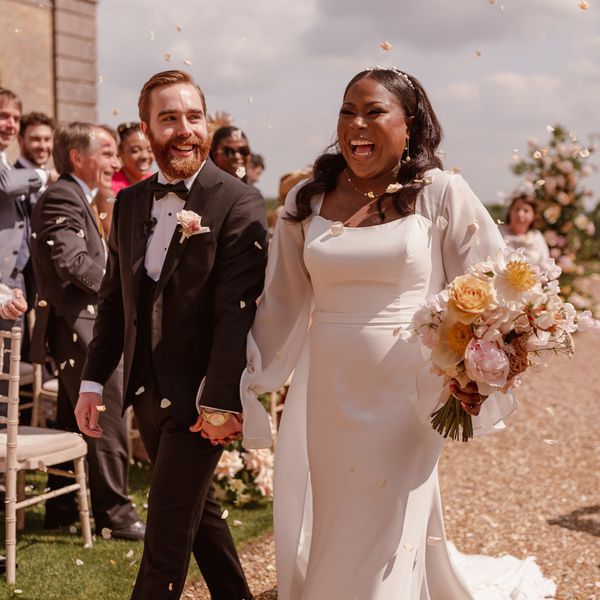 Bride and groom holding hands and smiling during the recessional while guests toss flower petals