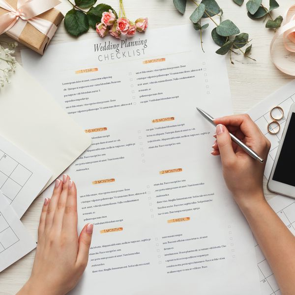 Woman holding a pen over a wedding planning checklist surrounded by calendar sheets and packages