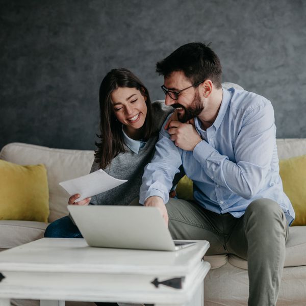 Couple smiling while looking at their laptop screen and holding papers