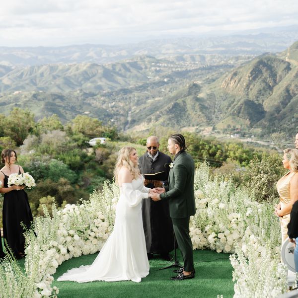 Bride in Off the Shoulder Wedding Dress and Groom in Green Suit Exchanging Vows on Mountaintop