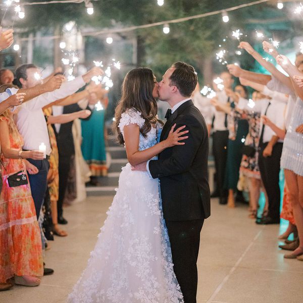 Bride and groom kissing while their guests form a tunnel with lit sparklers outside