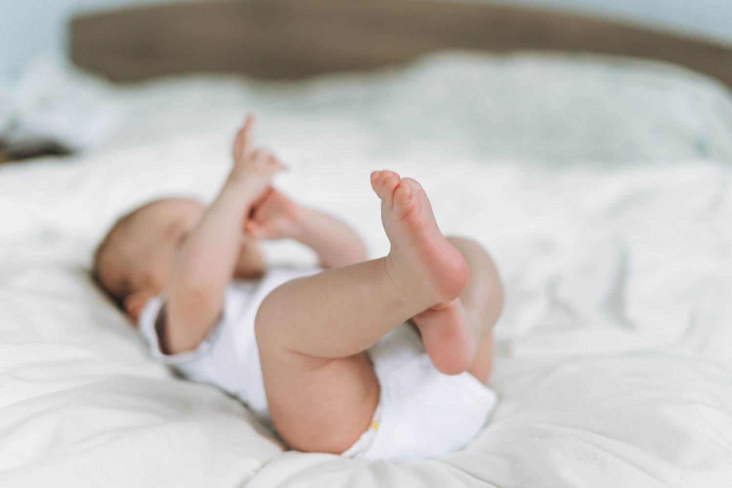 Baby in Onesie Lying on White Bed Linens