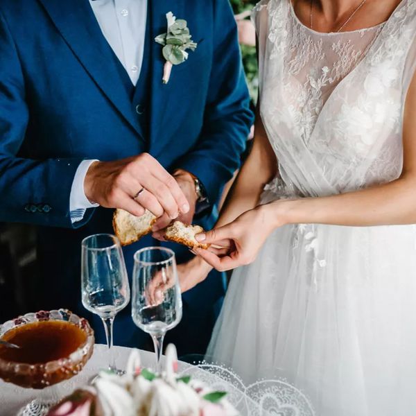 Bride in a white wedding dress and groom in a navy blue suit breaking bread during their wedding ceremony.