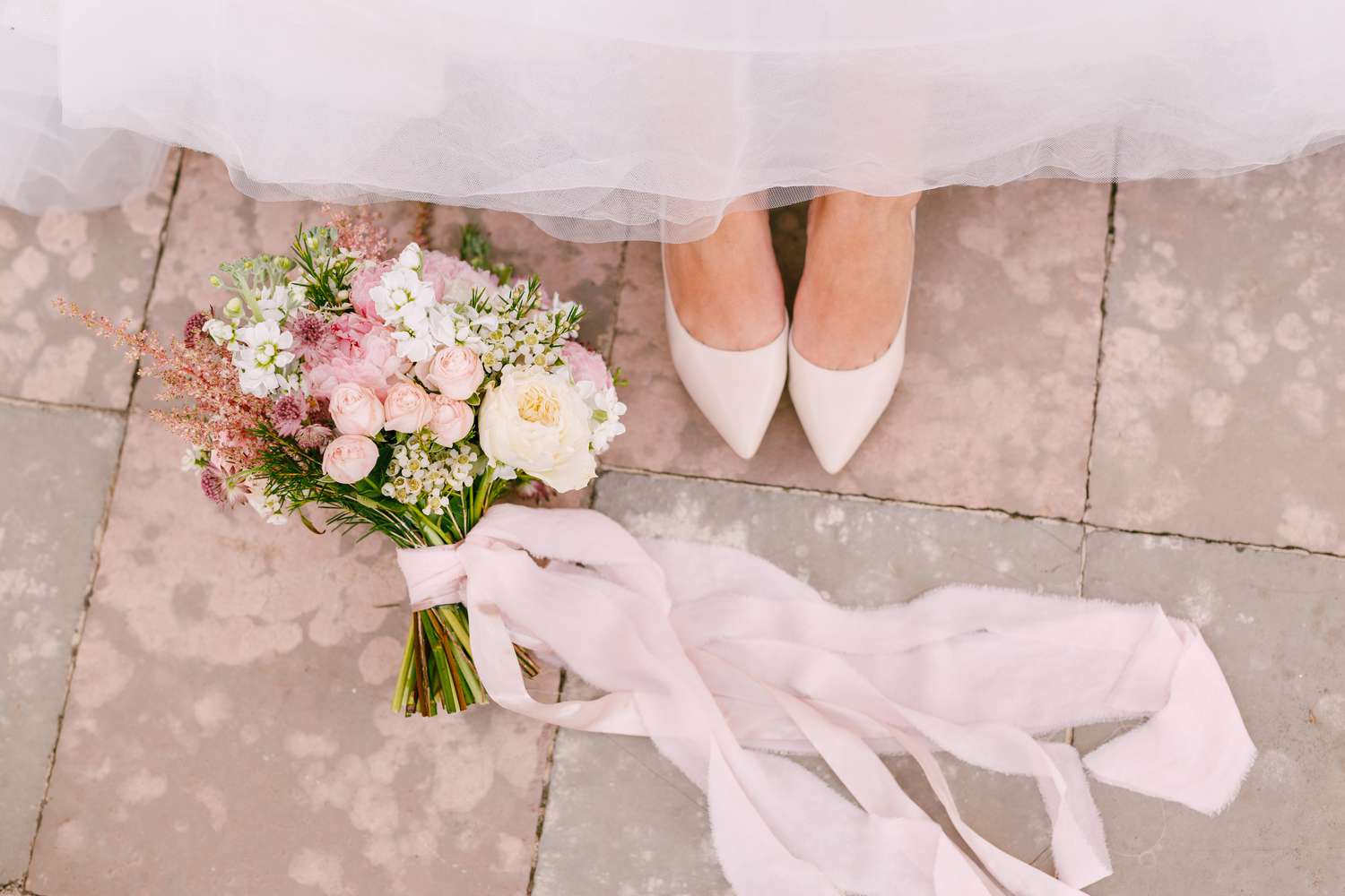Closeup of Bride's White Shoes and Colorful Wrapped Bouquet on the Floor