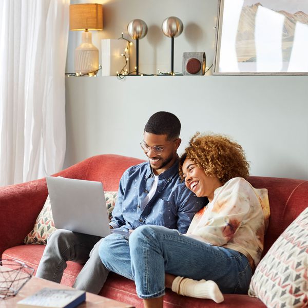 Couple sitting on the couch, laughing and looking at a laptop screen