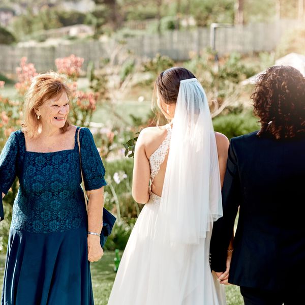 Smiling Older Woman in Blue Dress Looking at Bride and Groom With Natural Background