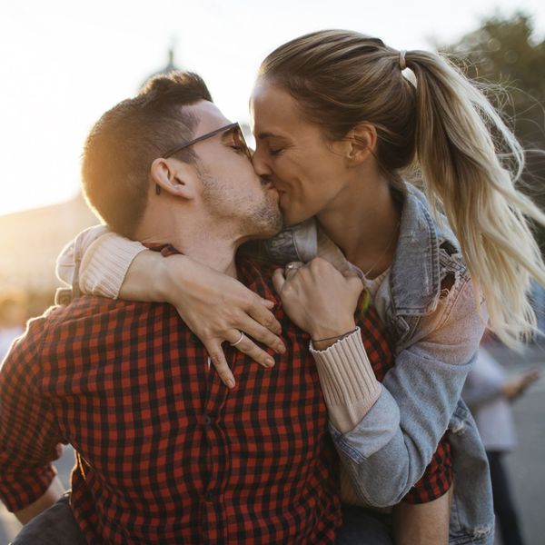 Young Couple Kissing During Piggyback Ride Outside at Sunset
