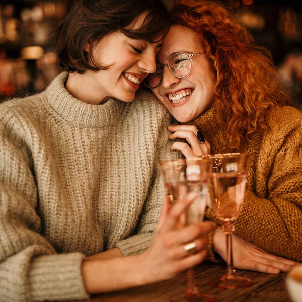 Attractive Young Female Couple Cuddling at a Bar While Holding Wine Glasses