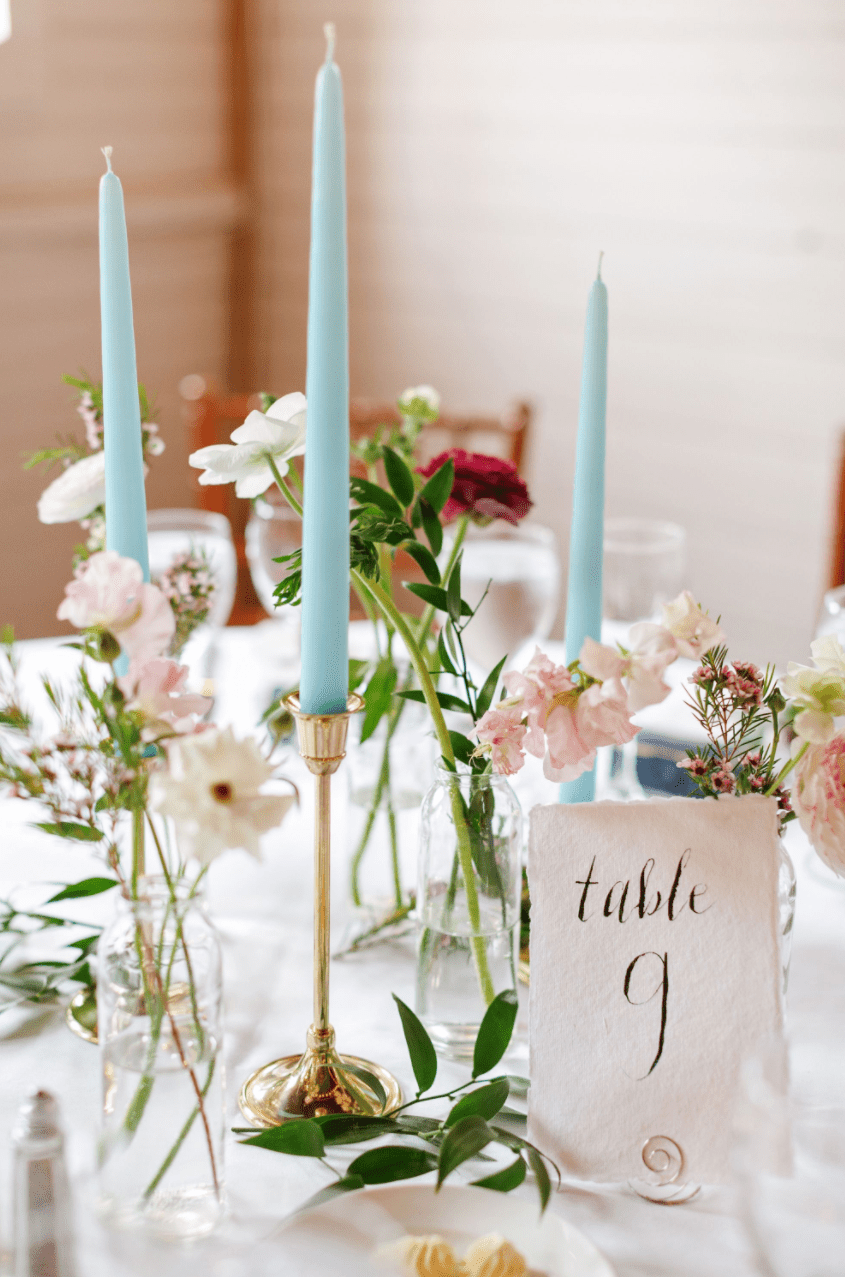 Blue taper candles on gold candlestick surrounded by bud vases of colorful flowers