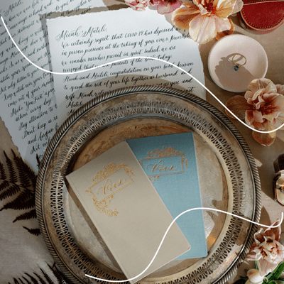 ceremony script in cursive on deckled edge paper with peach flowers, ring, and vow cards on silver charger,