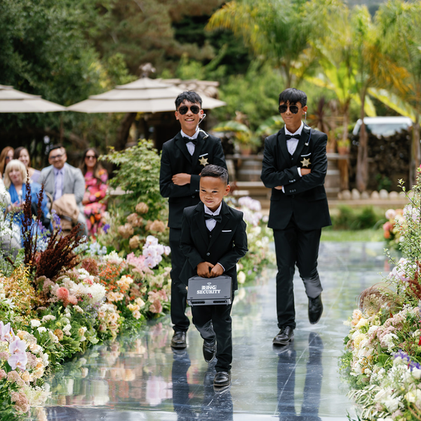 Young ring bearer carrying a ring security box down the aisle with two older ring bearers dressed as security guards trailing behind him