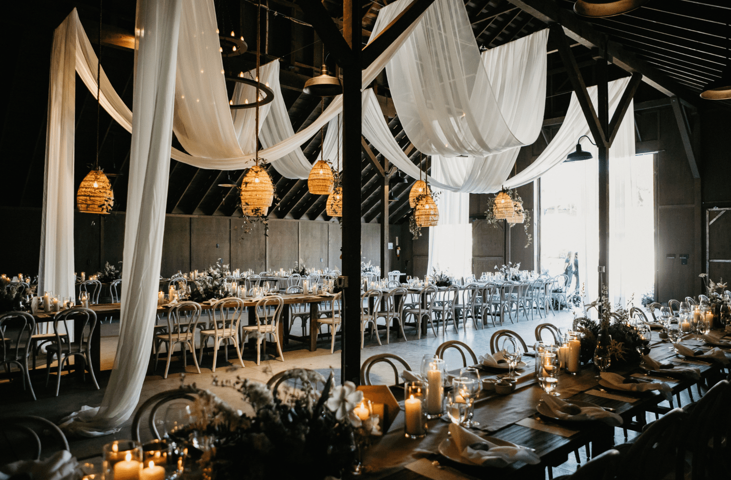Barn interior with soaring ceilings softened by white draped linens and rattan lanterns